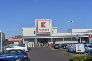 Widok na sklep Kaufland z parkingiem, błękitne niebo w tle, klienci przy wejściu.