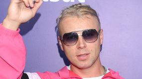 Skolim w różowym dresie i okularach przeciwsłonecznych, z ustawioną ręką.
