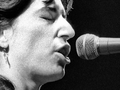 Patti Smith - 1979 rok. Kobieta śpiewa do mikrofonu, zamknięte oczy, skupiona na występie. Czarnobiałe zdjęcie.