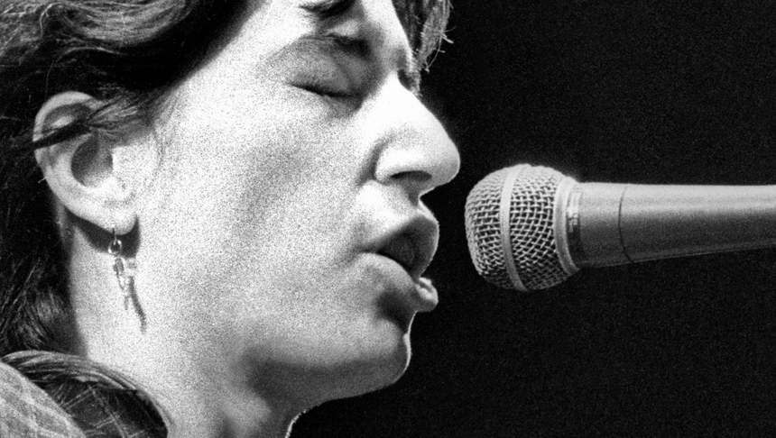 Patti Smith - 1979 rok. Kobieta śpiewa do mikrofonu, zamknięte oczy, skupiona na występie. Czarnobiałe zdjęcie.