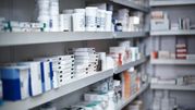 Zdjęcie przedstawia półki w aptece z różnymi lekami i opakowaniami farmaceutycznymi.