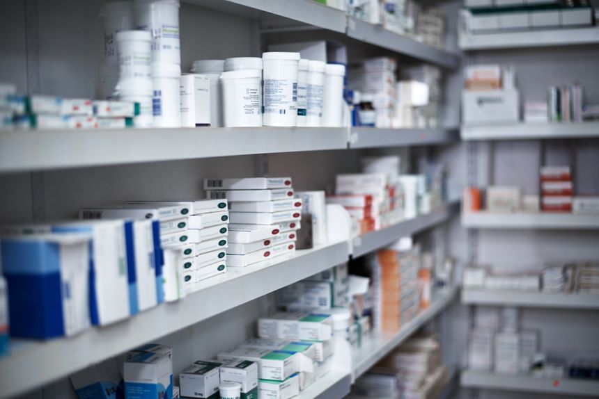 Zdjęcie przedstawia półki w aptece z różnymi lekami i opakowaniami farmaceutycznymi.
