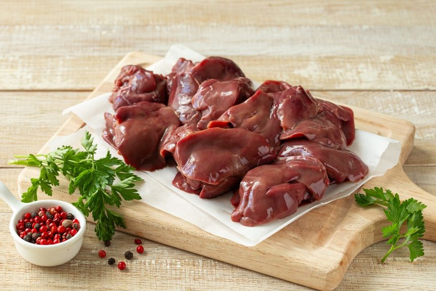 Na drewnianej desce leży surowa wątróbka, obok świeże zioła i przyprawy.