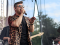 Mężczyzna w okularach słonecznych śpiewa na scenie, ubrany w kolorową koszulę w leoparda.