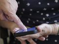 Osoba dotyka ekranu smartfona jedną ręką, druga leży na kolanach.