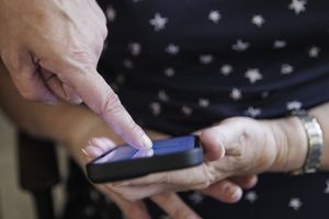 Osoba dotyka ekranu smartfona jedną ręką, druga leży na kolanach.