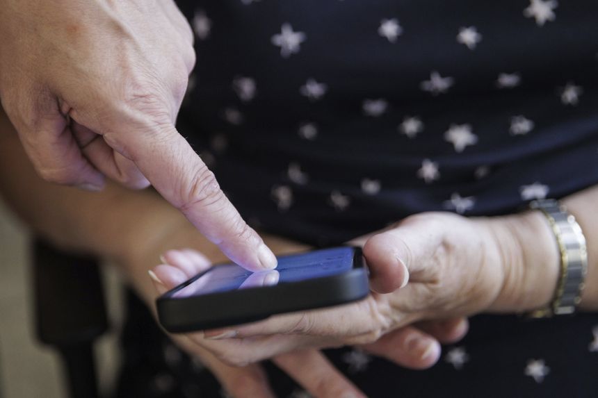 Osoba dotyka ekranu smartfona jedną ręką, druga leży na kolanach.
