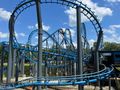 Zjeżdżalnia rollercoastera z niebieskimi torami na tle jasnego nieba z chmurami.