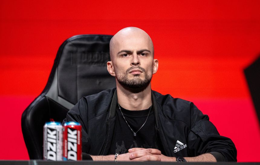 Blendusiak w czarnej kurtce, siedzi z poważnym wyrazem twarzy, przed nim napoje.