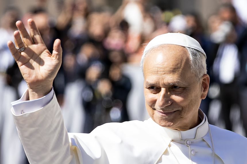 Papież uśmiechnięty, machający ręką do tłumu w słonecznym dniu. W tle zgromadzeni ludzie.