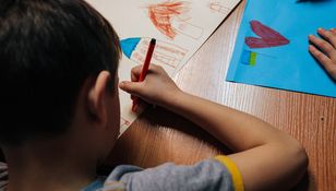 Dziecko rysujące kredką na dużym arkuszu papieru, obok kolorowe rysunki.