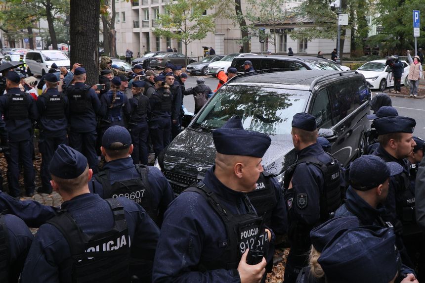 Grupa policjantów w mundurach, zabezpieczająca teren wokół czarnego minivana.