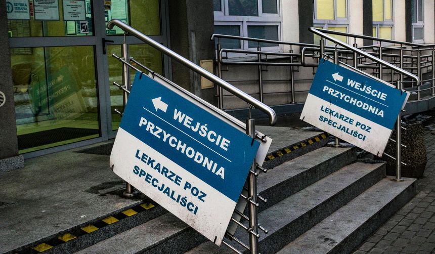 Przybudówka przychodni z niebieskimi znakami wskazującymi wejście i lekarzy specjalistów.