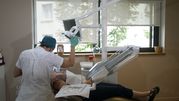 Dentysta wykonuje zabieg w komfortowym gabinecie stomatologicznym. Pacjent leży na fotelu.