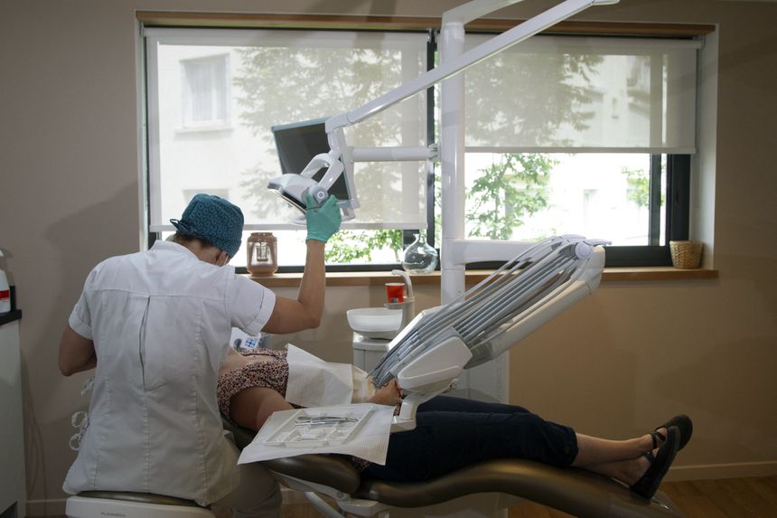 Dentysta wykonuje zabieg w komfortowym gabinecie stomatologicznym. Pacjent leży na fotelu.