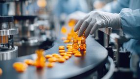 Pracownik w rękawiczkach umieszcza kapsułki w szklanych butelkach na linii produkcyjnej.
