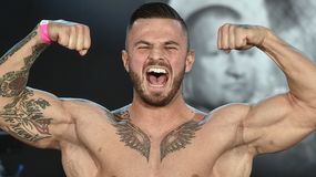 Erko Jun z tatuażami, ubrany w różowy opaskę, intensywnie pokazuje mięśnie i krzyczy.