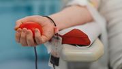 Zdjęcie przedstawia dłoń trzymającą czerwoną kulę podczas oddawania krwi.