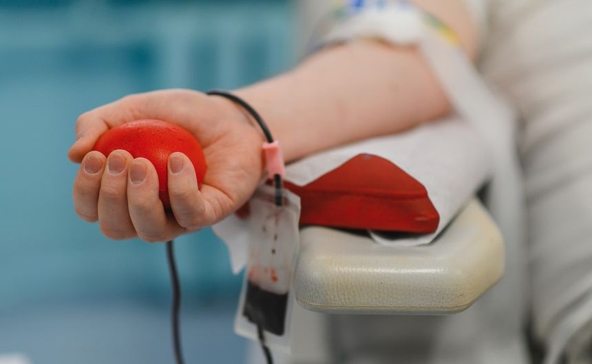 Zdjęcie przedstawia dłoń trzymającą czerwoną kulę podczas oddawania krwi.