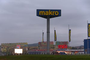 Widzok sklepy Makro i Tesco, w tle kolorowe bloki mieszkalne, szare niebo.