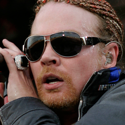 Axl Rose w 2006 roku. Osoba z okularami przeciwsłonecznymi i warkoczkami trzyma mikrofon, intensywnie śpiewa.