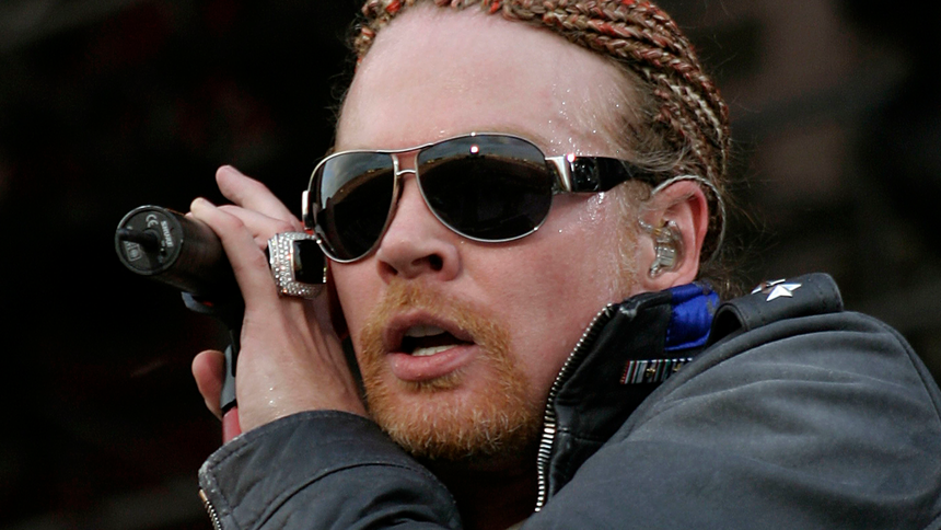 Axl Rose w 2006 roku. Osoba z okularami przeciwsłonecznymi i warkoczkami trzyma mikrofon, intensywnie śpiewa.