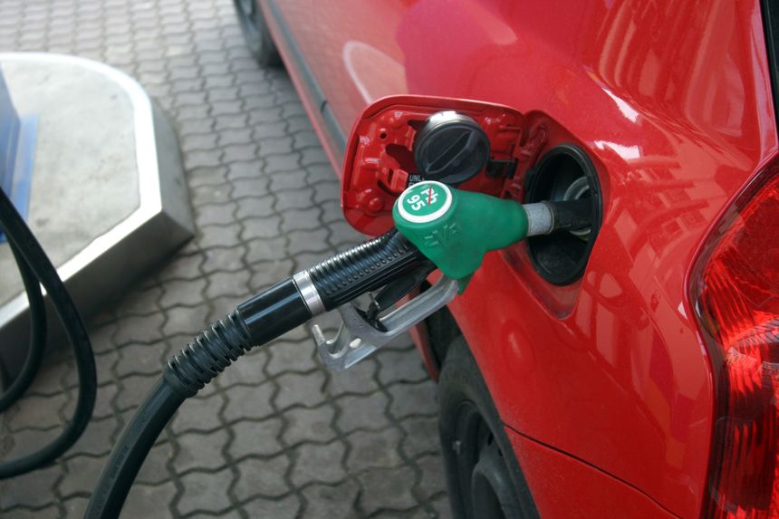 Zdjęcie przedstawia końcówkę dystrybutora paliwa włożoną w czerwone auto na stacji benzynowej.