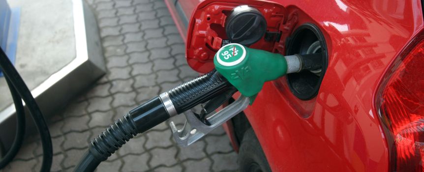 Zdjęcie przedstawia końcówkę dystrybutora paliwa włożoną w czerwone auto na stacji benzynowej.