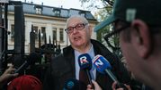 Mężczyzna w okularach, przemawia przed grupą dziennikarzy przy metalowym ogrodzeniu.