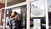 Na zdjęciu mężczyzna stoi przed drzwiami placówki NFZ, spoglądając w kierunku wejścia.