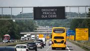 Na autostradzie widoczny żółty autobus oraz znaki informacyjne o pracach drogowych.