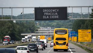 Na autostradzie widoczny żółty autobus oraz znaki informacyjne o pracach drogowych.