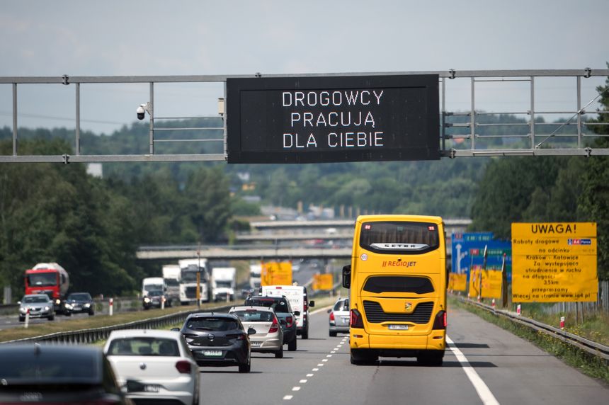 Na autostradzie widoczny żółty autobus oraz znaki informacyjne o pracach drogowych.