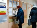 Dwie osoby w kurtkach czekają przy okienku rejestracyjnym w placówce medycznej.