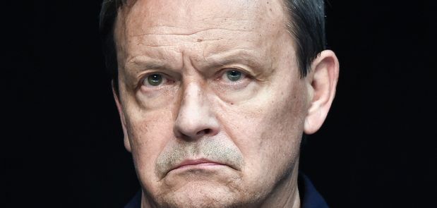 Mężczyzna z poważnym wyrazem twarzy, ciemne tło, wyraźne rysy twarzy.