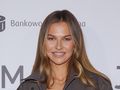 Anna Lewandowska z długimi włosami, uśmiecha się na tle jasnego tła z logo.