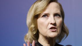 Izabela Kuna z krótkimi, blond włosami, mówi do mikrofonu w eleganckiej bluzce.