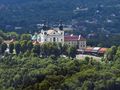 Widok na klasztor w zielonym otoczeniu, z drzewami i budynkami w tle, w pogodny dzień.