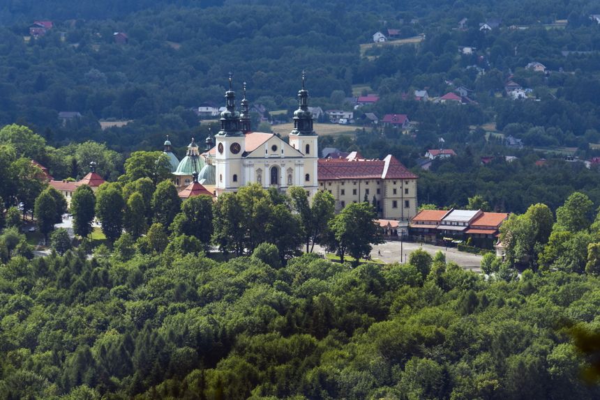 Widok na klasztor w zielonym otoczeniu, z drzewami i budynkami w tle, w pogodny dzień.