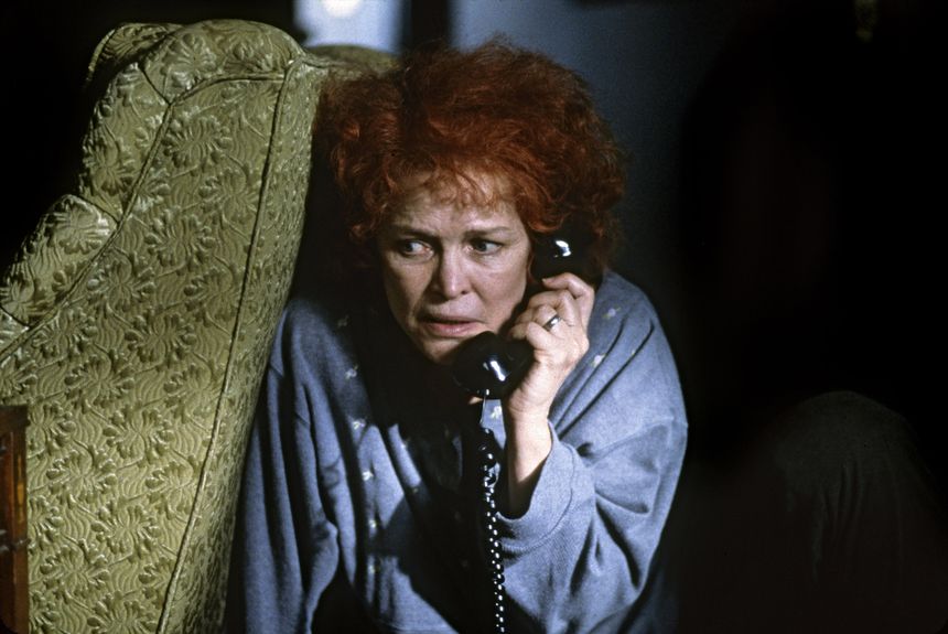 Na zdjęciu zdenerwowana kobieta rozmawia przez telefon, siedząc obok ozdobnej sofy.