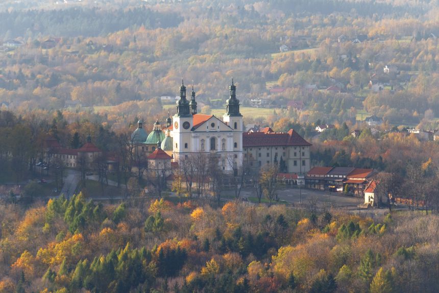 Widok na zabytkowy klasztor otoczony jesiennymi drzewami i pejzażem górskim.