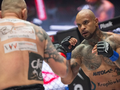 Dwóch zawodników MMA w ringu, skupionych na walce, jeden z nich ma tatuaże.