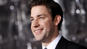 Mężczyzna w garniturze uśmiecha się, na tle rozmytych świetlnych refleksów.