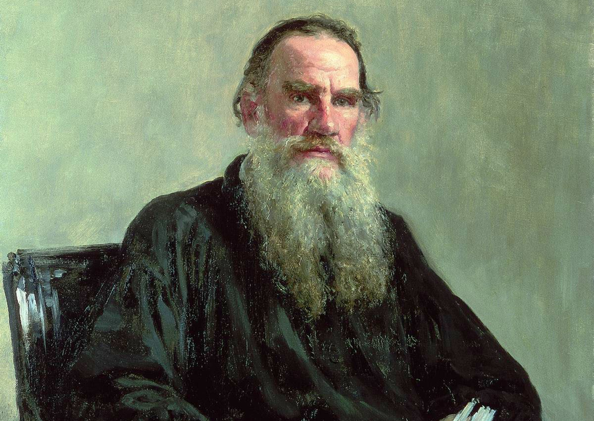 Na zdjęciu portret mężczyzny z długą brodą, w czarnym ubraniu, siedzącego na krześle.