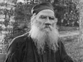 Mężczyzna z długą brodą, w tradycyjnym stroju, siedzi w cieniu drzew. Czarno-biała fotografia.