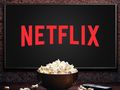 Na zdjęciu ekran telewizora z logo Netflix oraz miską popcornu na stole.