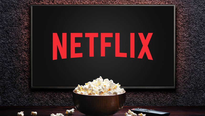 Na zdjęciu ekran telewizora z logo Netflix oraz miską popcornu na stole.