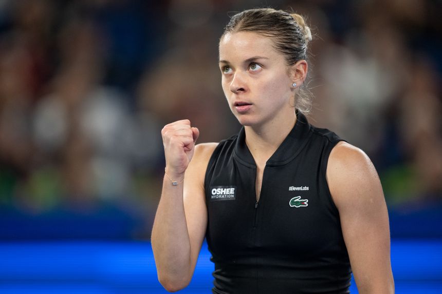 Kobieta sportowiec z czarnym topem, z płaszczyzną na tle, podnosi zaciśniętą pięść w geście triumfu.