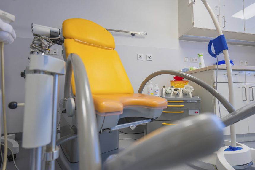 Fotele dentystyczny w gabinecie, sprzęt medyczny i półki z artykułami higienicznymi.