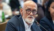 Mężczyzna z siwą brodą i okularami, siedzący przy stole konferencyjnym.